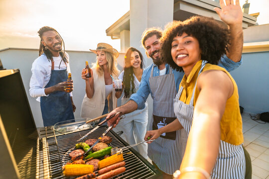 Happy friends taking selfie and grilling food, drinking beer on rooftop