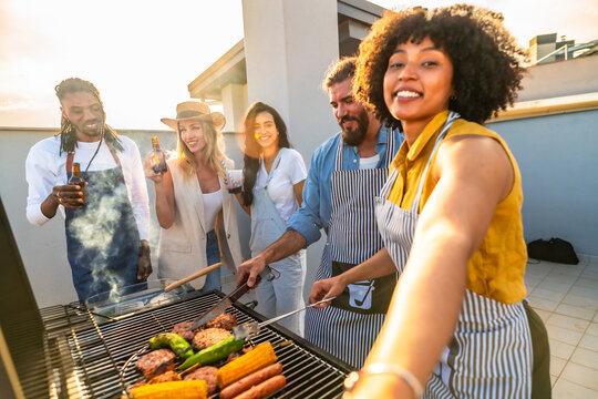 Happy friends making barbecue and taking selfie on rooftop