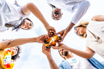 Friends toasting with beer bottles at beach party, celebrating summer together
