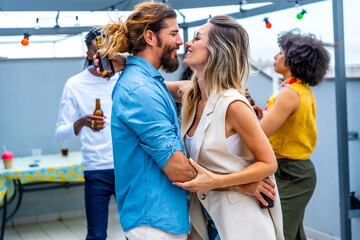 Couple embracing at rooftop party with friends enjoying drinks