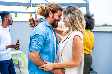 Couple embracing at rooftop party with friends enjoying drinks