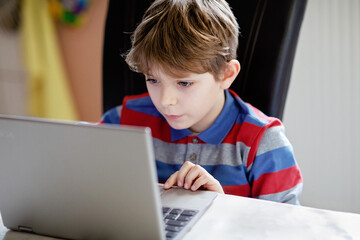 Happy healthy kid boy with glasses making school homework at home with notebook. Interested child...