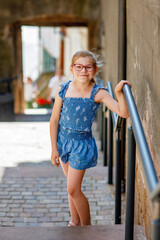 Little school girl with eyeglasses wearing a summer outfit walking in the city on a warm day. Real...