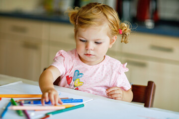 Cute adorable baby girl learning painting with pencils. Little toddler child drawing at home, using...
