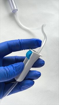 A woman's hand in a medical glove holds an infusion system on a white background. The doctor regulates the rate of administration of the solution. Intravenous infusion of medication.