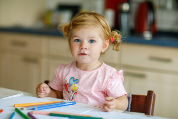 Cute adorable baby girl learning painting with pencils. Little toddler child drawing at home, using...