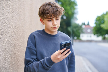 Portrait of smiling teenage schoolboy holding a smartphone. Happy teen boy talking to friends on video call, looking confidently at the camera. Real life, real people, youth lifestyle concept.