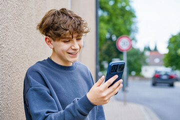 Portrait of smiling teenage schoolboy holding a smartphone. Happy teen boy talking to friends on video call, looking confidently at the camera. Real life, real people, youth lifestyle concept.