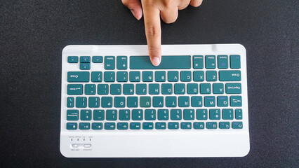 Top view of finger pressing space button of a green wireless computer keyboard isolated on black...