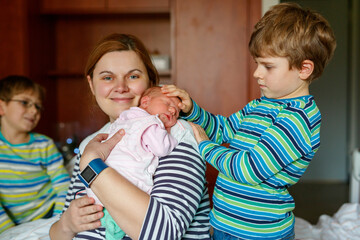 Mother holding newborn baby girl in hospital bed, with two sons sitting beside her. Real life, real people moment of family love, siblings bonding, and joy of welcoming a new child.