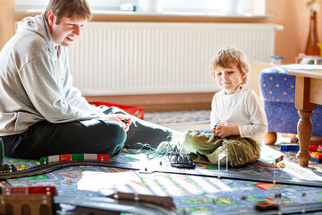 Father and son playing with racing cars on racetrack, indoors, with cars. Happy little preschool boy and young man having fun with indoor race game