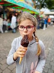 Little girl eating a big chocolate ice cream in a cone at a fair