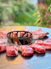 Many pieces of juicy beef steaks sizzling on a barbecue grill. Fresh meat cooking outdoors for a summer BBQ. Real life, real people, food preparation and grilling concept