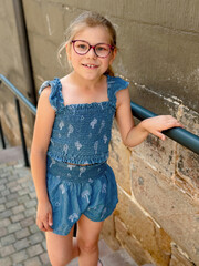 Little school girl with eyeglasses wearing a summer outfit walking in the city on a warm day. Real life, real people moment of childhood, style, and everyday urban lifestyle.