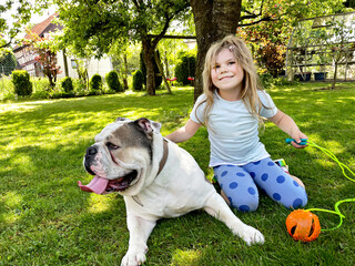 Cute little toddler girl playing with family dog in garden. Happy smiling child having fun with dog, hugging playing with ball. Happy family outdoors. Friendship and love between animal and kids