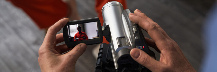 Caucasian man holding video camera recording woman in orange prison uniform standing indoors, focus...