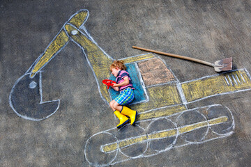 Happy little boy drawing an excavator with colorful chalk outdoors in summer. Real life, real people moment of creativity, imagination, and fun childhood playtime on the pavement.