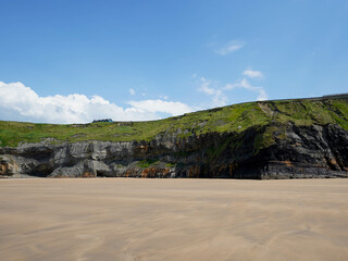 A wide sandy beach stretches beneath green cliffs under a clear blue sky