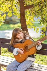 Child playing guitar under sunny tree in park