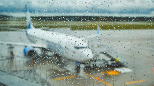 Raindrops blurring airplane view while parked on wet airport tarmac during rainfall