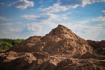 Construction site featuring a large mound of dirt under a blue sky with fluffy clouds in the afternoon