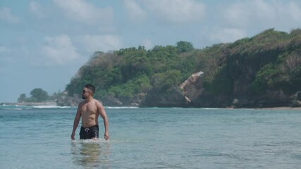 A man enjoys a peaceful day at a crystal clear blue beach in Bali walking on water, laying on sand, and listening to music while relaxing by the sea. - Powered by Adobe