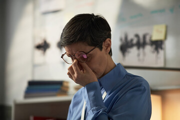 Middle aged Caucasian woman standing indoors pinching bridge of nose with eyes closed appearing...