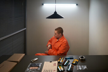 Caucasian young adult woman wearing orange prison uniform sitting alone in interrogation room...
