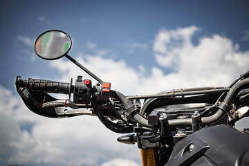 Close view of motorcycle handlebar with mirror and throttle under blue sky