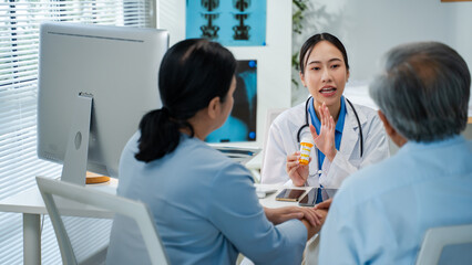Asian woman Doctor Explaining Prescription Medication to Senior Patients.asian doctor discusses medication instructions while holding a prescription bottle,attentively guiding couple elderly patients