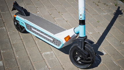 Bright electric scooter parked on a brick pathway in an urban area during daylight