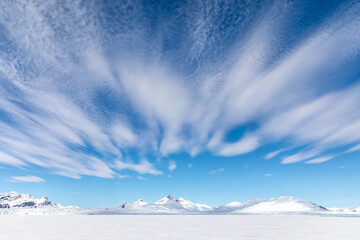 Cloudscape in Svalbard with snowy mountain peaks and fluffy white clouds in a blue summer sky....