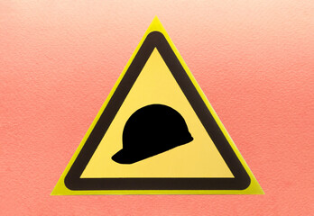 Construction helmet in a yellow triangle close-up on a light background. Warning sign about the...