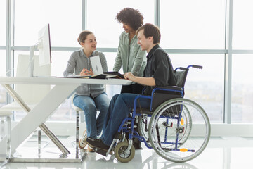 Teamwork brainstorm. Diverse multiracial colleagues man in chair for people with disability working together. Group of people sitting in creative office discussing business. Young professional team