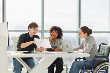 Teamwork brainstorm. Diverse multiracial colleagues woman in chair for people with disability working together. Group of people sitting in creative office discussing business. Young professional team