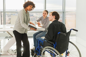 Teamwork brainstorm. Diverse multiracial colleagues man in chair for people with disability working together. Group of people sitting in creative office discussing business. Young professional team