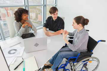 Teamwork brainstorm. Diverse multiracial colleagues woman in chair for people with disability working together. Group of people sitting in creative office discussing business. Young professional team