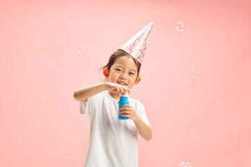 Cute Child Girl Blowing Soap Bubbles During Herself Birthday Standing on Pink Isolated