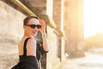 Portrait young adult elegant woman black dress and sunglasses smiles confidently in golden sunlight...