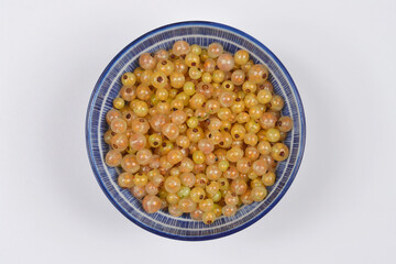 A blue and white patterned bowl is filled with a generous amount of fresh, translucent white currants, viewed from directly above on a light background