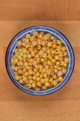 A blue and white patterned bowl, filled with fresh, translucent white currants, is prominently displayed on a wooden surface from a top-down perspective