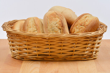 A rustic woven basket is filled with several freshly baked, golden-brown bread rolls, set on a...