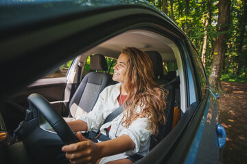 Happy young curly woman is driving a car during summer travel