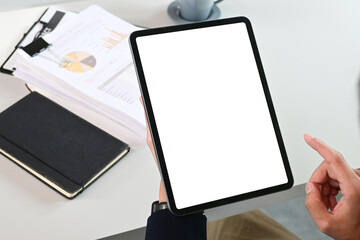 A person is holding a tablet with a white screen and a black book on the table. The tablet is pointing to a tablet