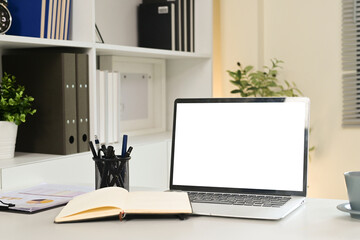 A laptop sits on a desk with a notebook and a cup of coffee. The laptop is open to a blank screen