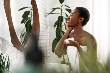 Woman applying skincare in a bright bathroom filled with plants during a morning routine