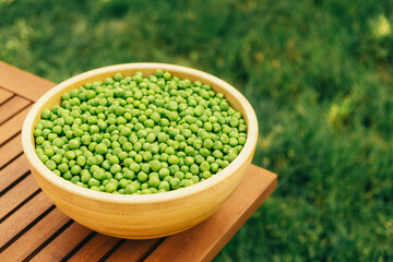 A vibrant and colorful bowl filled with fresh green peas is beautifully arranged on a wooden table outside