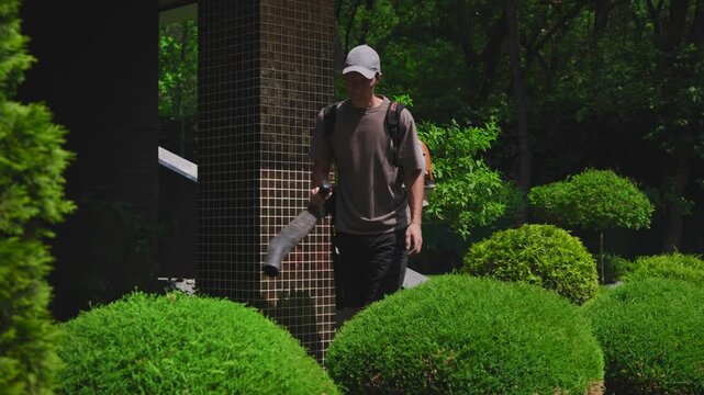 Gardener using professional leaf blower to clear foliage from shrubs and plants. Essential landscape maintenance for pristine garden design.