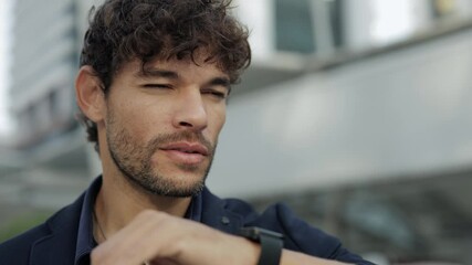 Portrait of positive Hispanic businessman talks via smartwatch and stands on street closeup. Latin man entrepreneur uses digital wristwatch to call client at corporate building - Powered by Adobe