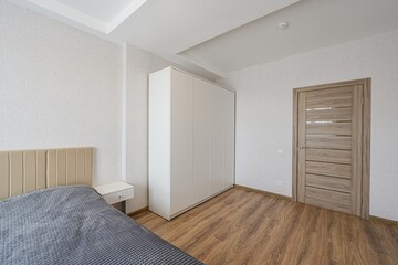 bright bedroom featuring a bed, white wardrobe, and a wooden door. Walls are light with a subtle pattern and there's wooden flooring